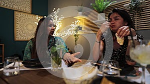 Closeup view of two females eating and talking in a cafe with plants and light decorations