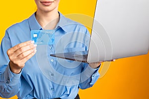 Closeup view of woman in the blue shurt holding laptop and credit card.