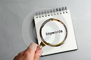 Closeup view of woman holding magnifier glass over empty notebook at grey stone table. Find keywords concept