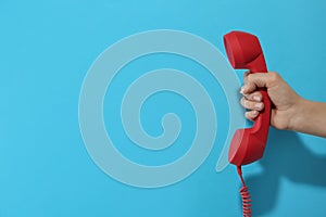 Closeup view of woman holding red corded telephone handset on light blue background, space for text. Hotline concept