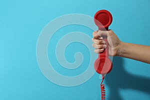 Closeup view of woman holding red corded telephone handset on light blue background  space for text. Hotline concept