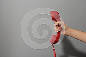 Closeup view of woman holding red corded telephone handset on light grey background, space for text. Hotline concept