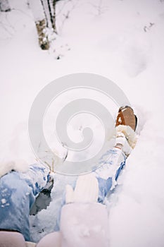 Closeup view of woman legs in jeans and winter boots sitting in the snow
