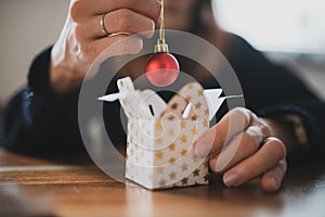 Closeup view of a woman placing shiny red holiday bauble in a small christmas giftbox