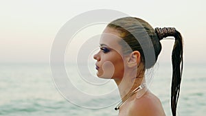 Closeup view of woman with professional golden makeup and wet ponytail walking by the water on the beach then