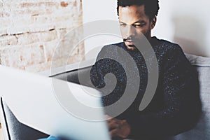 Closeup view of young African man using laptop while sitting sofa at his modern coworking studio.Concept full