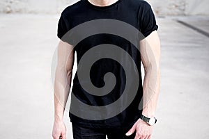 Closeup view of young muscular man wearing black tshirt and jeans posing outside. Empty background. Hotizontal mockup.