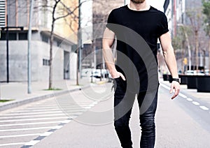 Closeup view of young muscular man wearing black tshirt and jeans walking on the streets of the modern city. Blurred