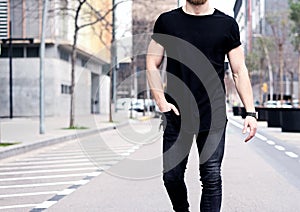 Closeup view of young muscular man wearing black tshirt and jeans walking on the streets of the modern city. Blurred photo