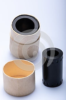 Closeup of a vintage 35mm film canister made out of cardboard with an old filmstrip in the foreground