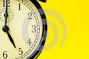 Closeup of a vintage analog black clock on a yellow background displaying 5 o`clock