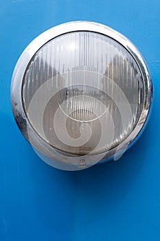 Closeup of a vintage train headlight with chrome trim on the blue surface