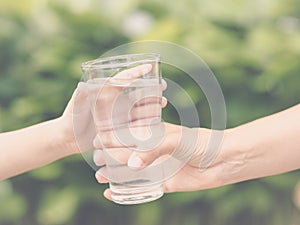 Closeup vintage woman hand giving glass of fresh water to child in the park.