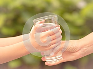 Closeup vintage woman hand giving glass of fresh water to child in the park.