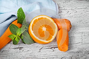 Closeup of vivid orange, slices of carrot and sappy green leaves of mint on a light wooden background.