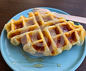 Closeup waffle topped with honey sauce on blue plate at cafe. Sweet bakery in dish on wooden table or background