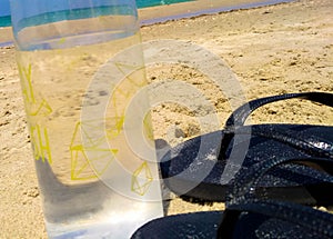 Closeup on Water bottle and black flip flops on a sand