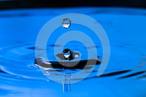 Closeup water drop falling and dripping from the top to the surface of water that makes two water drops. Water drop splash and