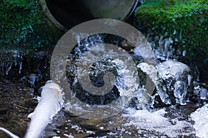 Closeup of water flowing from a big pipe outdoors, mossy stones blurred background