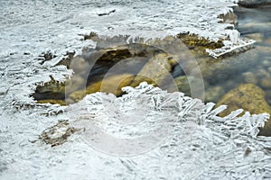 Closeup of water flowing in river, hole with crystalline ice around, long exposure makes flow silky smooth - winter weather