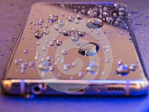 Closeup of waterdrops on a phone screen in neon light
