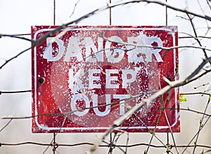 Closeup of weathered red Danger Keep Out sign posted to wire fen