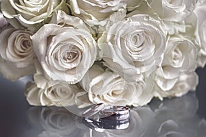 Closeup of a wedding bouquet next to wedding rings on glass