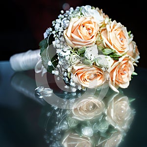 Closeup of a wedding bouquet next to wedding rings on glass