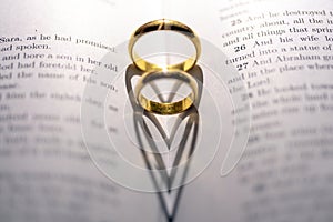 Closeup of wedding rings forming heart shapes on the bible - concept of love and marriage