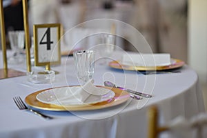 Closeup of wedding table dishes, plates with golden endings on a white tablecloth blurred background