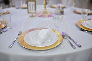 Closeup of wedding table dishes, plates with golden endings on a white tablecloth blurred background