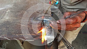 closeup of Welders hand doing gas weld with sparks flying as metal is being on a workbench at workshop