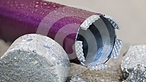 Closeup of wet purple core drill bit and cylindrical bored piece of gray concrete tile