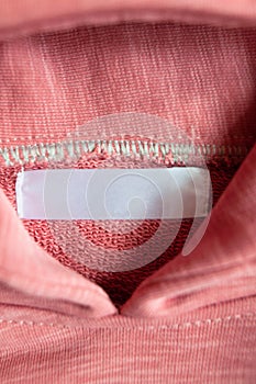 Closeup white blank clothing tag label on pink collar hoodie. Vertical photo. Selective focus