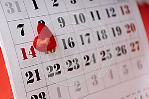 Closeup of white calendar page and red number 14 february.Valentines Day.Push pin and decorative heart on the calendar