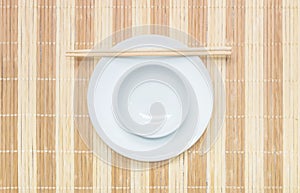 Closeup white ceramic chalice on circle dish and wood chopsticks on wood mat textured background on dining table in top view