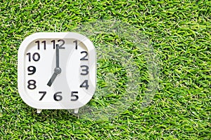 Closeup white clock for decorate in 7 o`clock on green artificial grass floor textured background with copy space