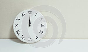 Closeup white clock for decorate show 12 a.m. on white wood desk and cream wallpaper textured background with copy space