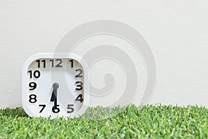 Closeup white clock for decorate show a half past six or 6:30 a.m. on green artificial grass floor and cream wallpaper textured ba photo
