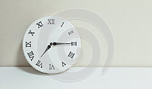 Closeup white clock for decorate show a quarter past seven or 7:15 a. m. on white wood desk and cream wallpaper textured backgroun