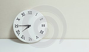 Closeup white clock for decorate show quarter to eight or 7:45 a.m. on white wood desk and cream wallpaper textured background wit