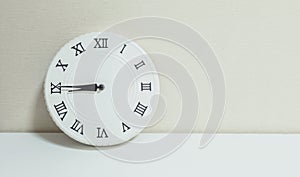 Closeup white clock for decorate show a quarter to nine or 8:45 a.m. on white wood desk and cream wallpaper textured background wi