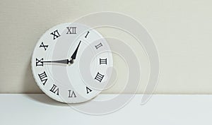 Closeup white clock for decorate show a quarter to one p.m. or 12:45 p.m. on white wood desk and cream wallpaper textured backgrou
