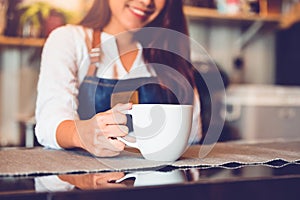 Closeup of white coffee cup with beautiful Asian woman barista background for serving to customer. Job and occupation. Food and