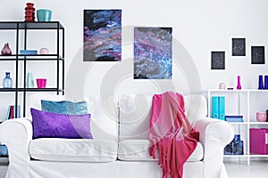 Closeup of white comfortable couch with pink blanket and purple and blue pillows in modern living room interior, real photo