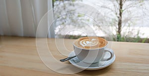 Closeup of white cup of hot coffee latte with milk foam art on wooden table