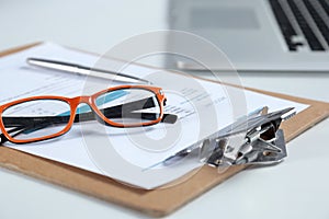 Closeup of white desktop with laptop, glasses, coffee cup, notepads and other items on blurry city background