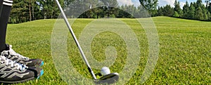 Closeup of white golf ball and club. Human feet on green grass