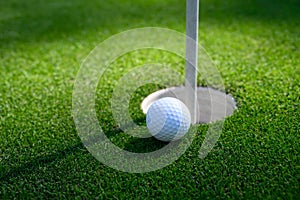 Closeup of white golf ball next to the cup on a putting green