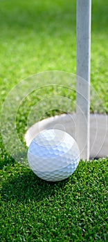 Closeup of white golf ball next to the cup on a putting green